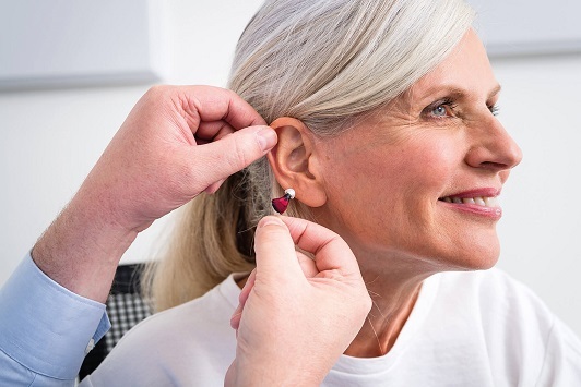 Seniorin mit grauen Haaren erhält von einem Hörakustiker ein modernes Hörgerät ins Ohr.